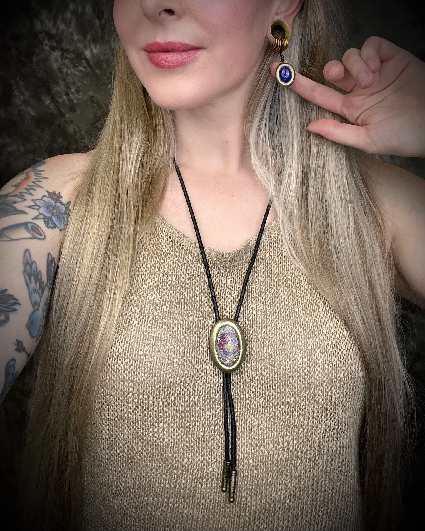 Model wearing Cadillac Ranch Fordite manmade colorful swirling gemstone Bolo tie set in a gold finish and mounted on soft black bolo leather. A talisman for the modern man, crystal jewelry for him. Western 2026 jewelry trend bolo. 