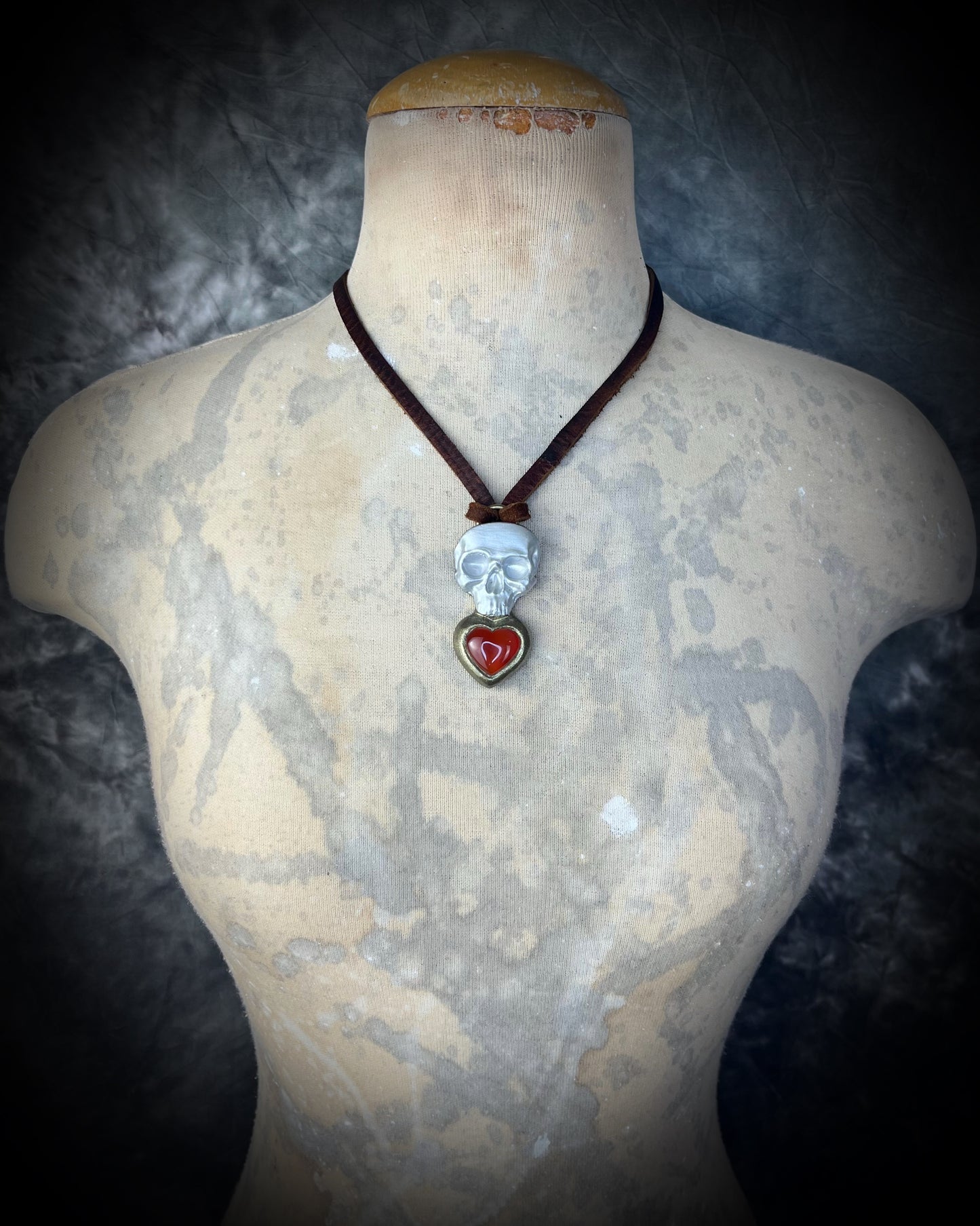 Model wearing pearl white skull and Carnelian heart talisman necklace on brown leather — witchy autumn statement jewelry.