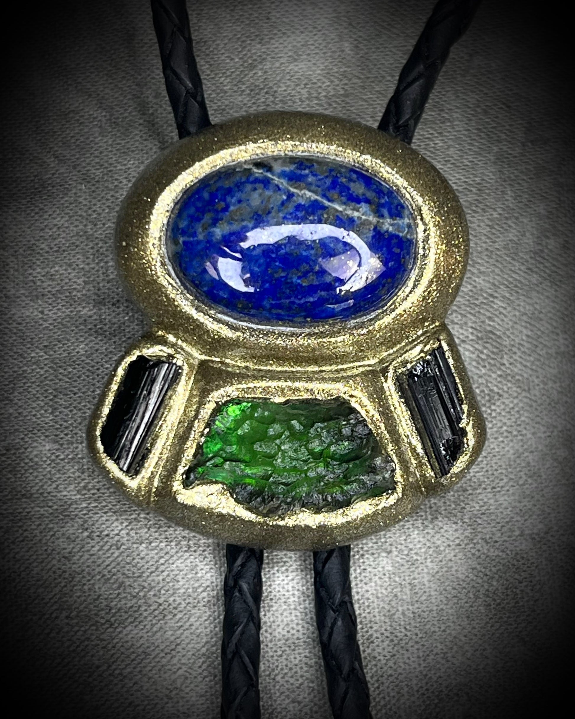Moldavite bolo tie with lapis lazuli and black tourmaline on black leather, featuring gold finish and spike bolo tips, handmade by Become Spellbound.