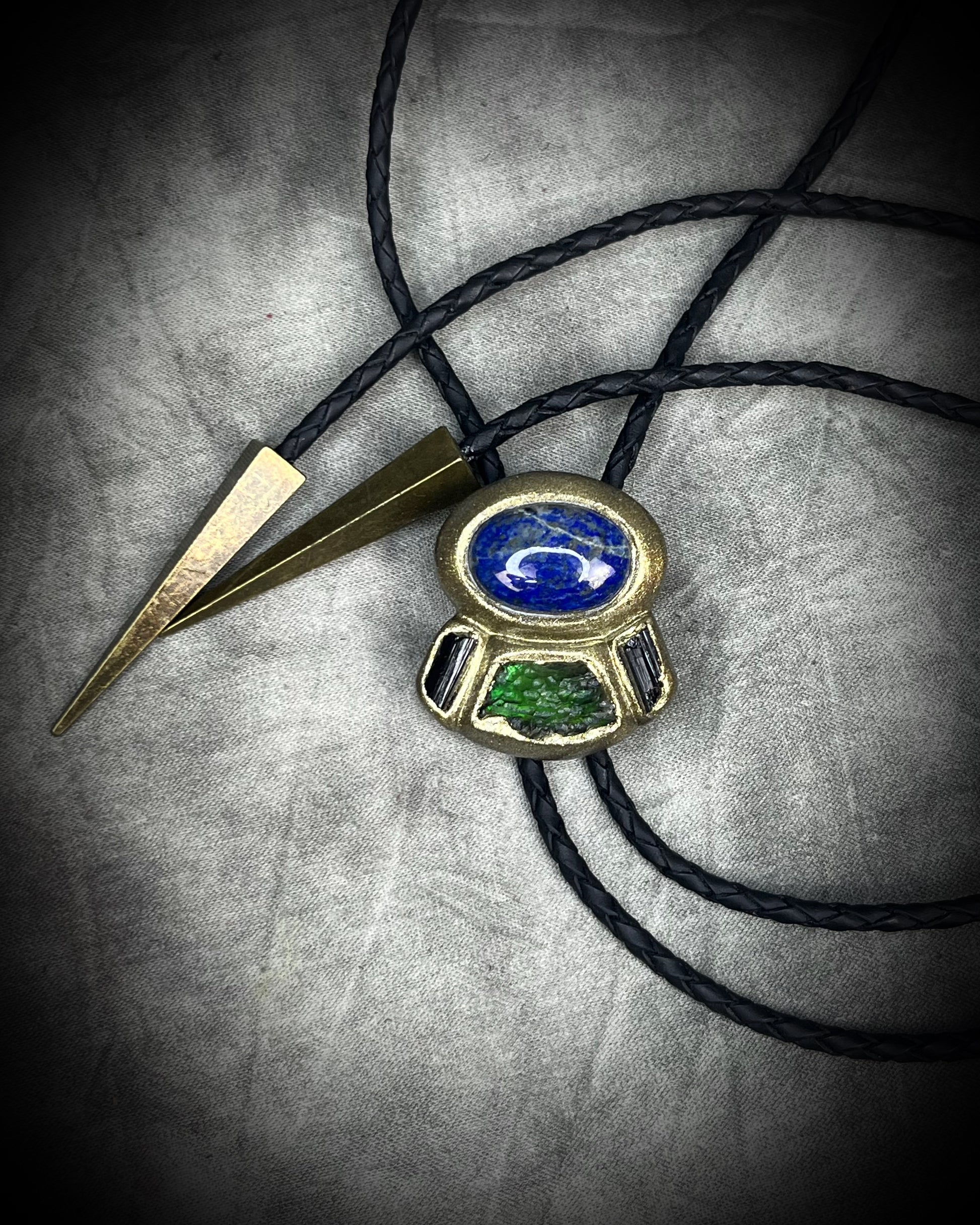 Moldavite bolo tie with lapis lazuli and black tourmaline on black leather, featuring gold finish and spike bolo tips, handmade by Become Spellbound.