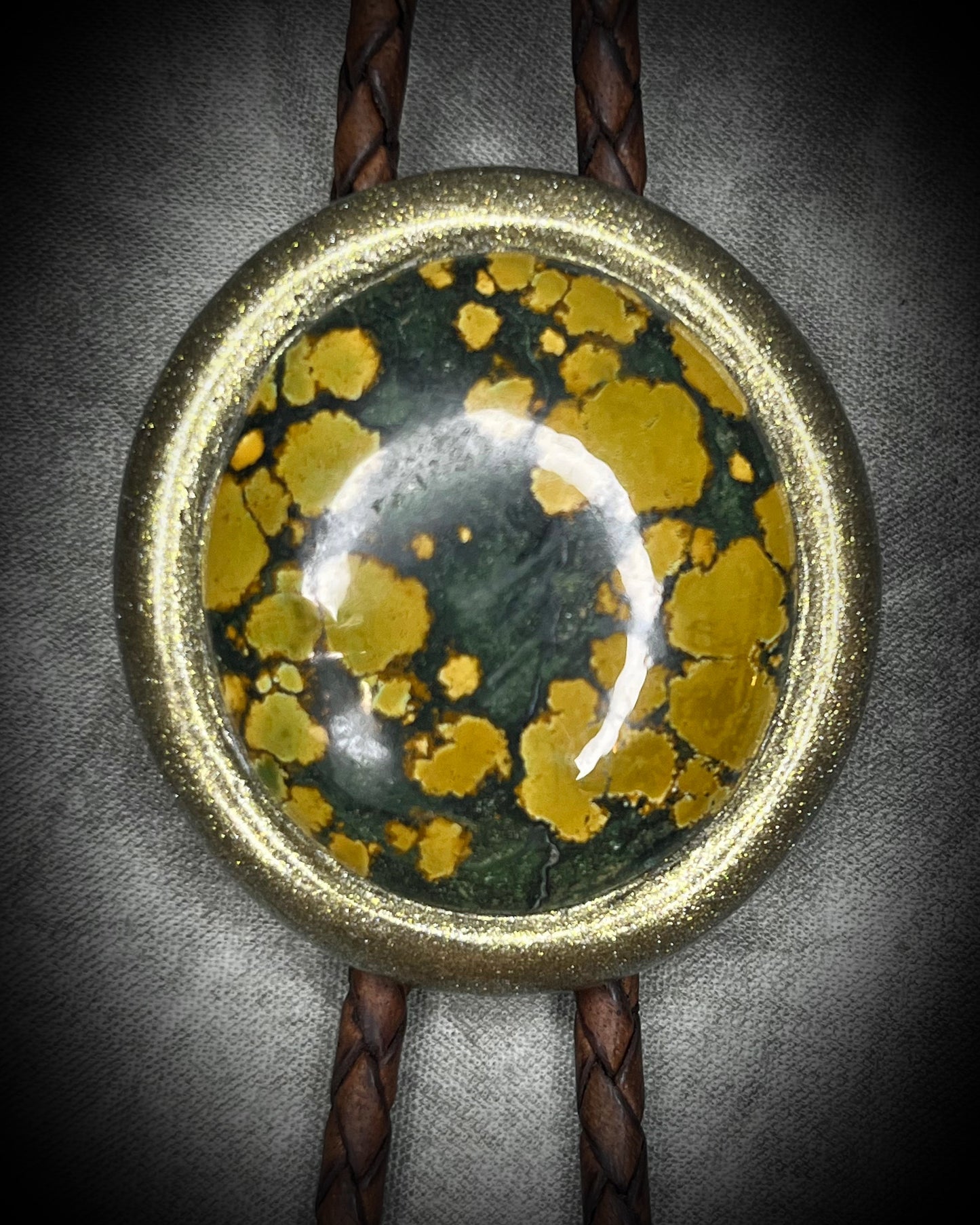 Mossy green and mustard-yellow turquoise bolo tie with natural plume markings, gold finish, brown leather, and gold spade tips.