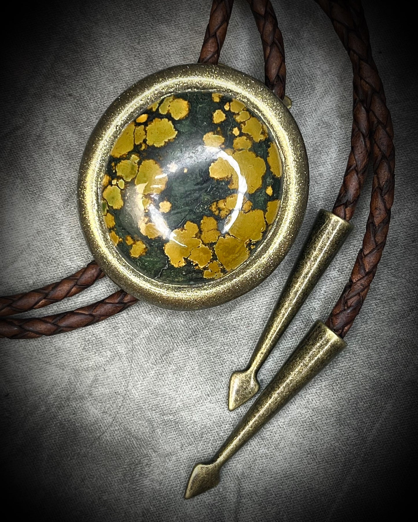 Mossy green and mustard-yellow turquoise bolo tie with natural plume markings, gold finish, brown leather, and gold spade tips.