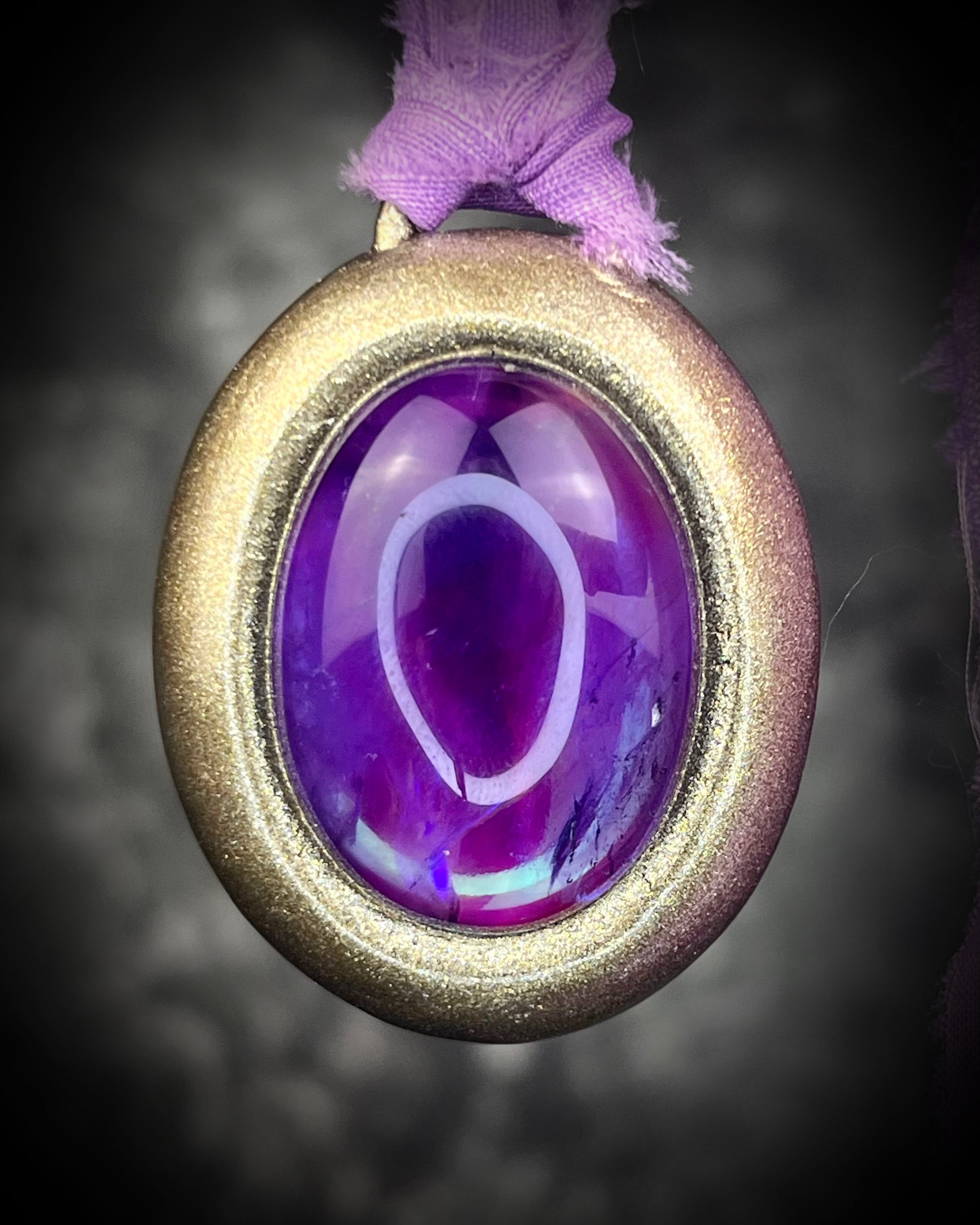 Mystical amethyst talisman with soft nebula glow, sculpted gold finish, and lilac recycled silk ties by Become Spellbound.