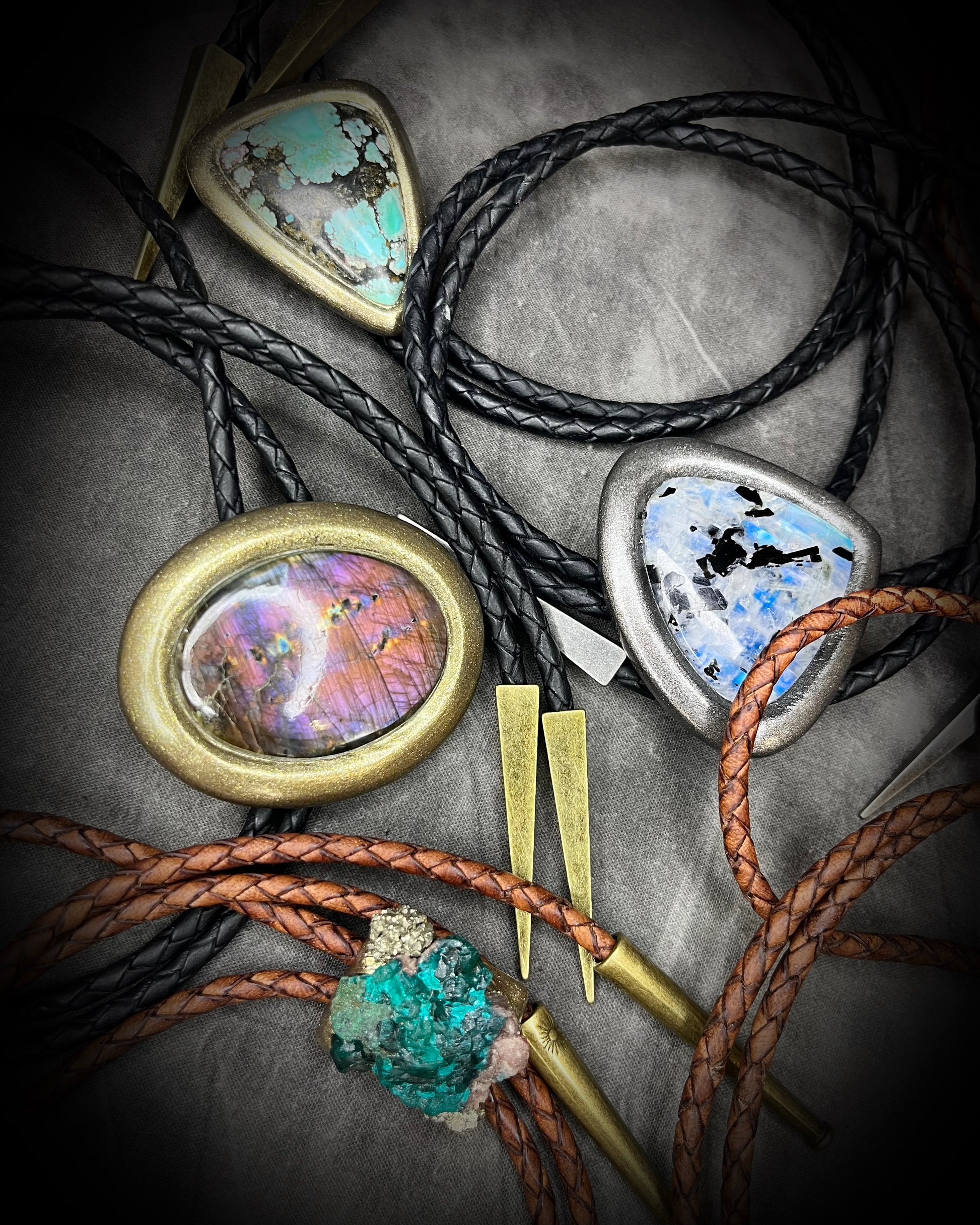Mystical crystal bolo ties with gold and silver finishes and black and brown leather on a textured background. Handmade western gift for him.