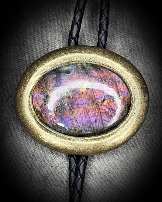 Mystical purple labradorite crystal bolo tie with a gold finish and black leather on a textured background. Handmade western gift for him.