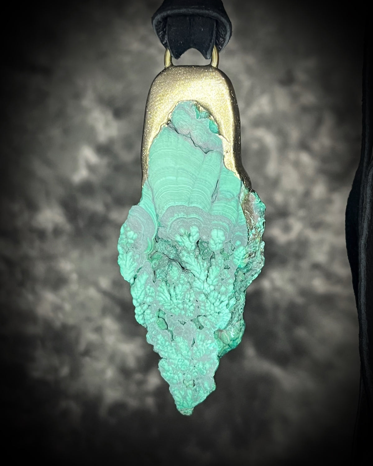 Natural malachite slab with distinctive green banding in a sculptural gold-finish talisman setting on black leather, handmade by Become Spellbound in Baltimore, Maryland.