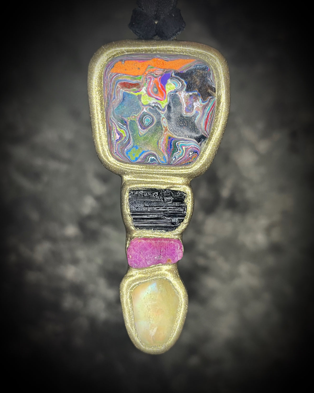 One-of-a-kind Cadillac Ranch Fordite talisman with hand-cut Fordite cabochon, black tourmaline, ruby, and Libyan Desert Glass in a gold-finish setting on black leather, handmade by Become Spellbound in Baltimore, Maryland.