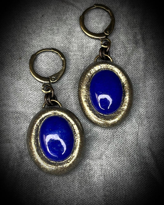 Pair of Lapis Lazuli earrings with blue oval gemstones and gold accents on brass huggie earring hooks. Regal statement earrings for wisdom and truth.