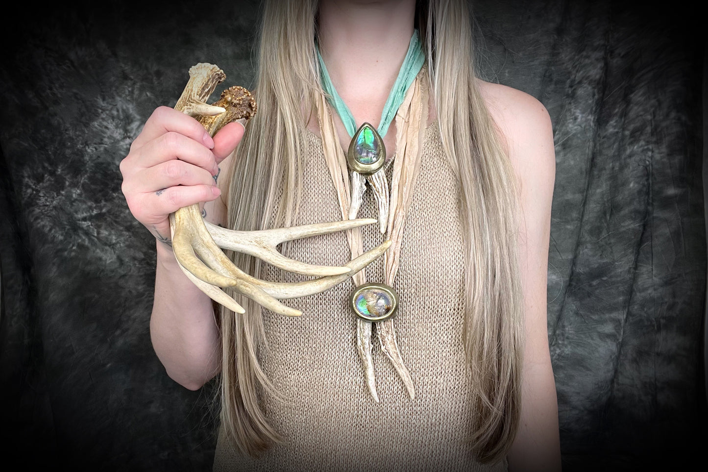 Person wearing a long, decorative necklace with antlers and crystals against a dark background
