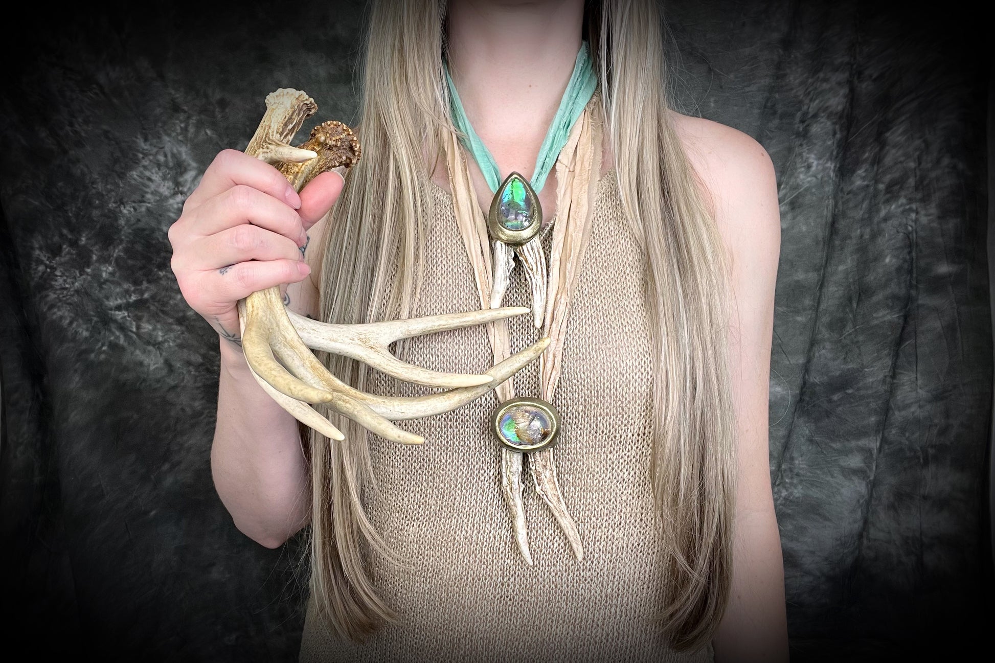 Person wearing a long, decorative necklace with antlers and crystals against a dark background