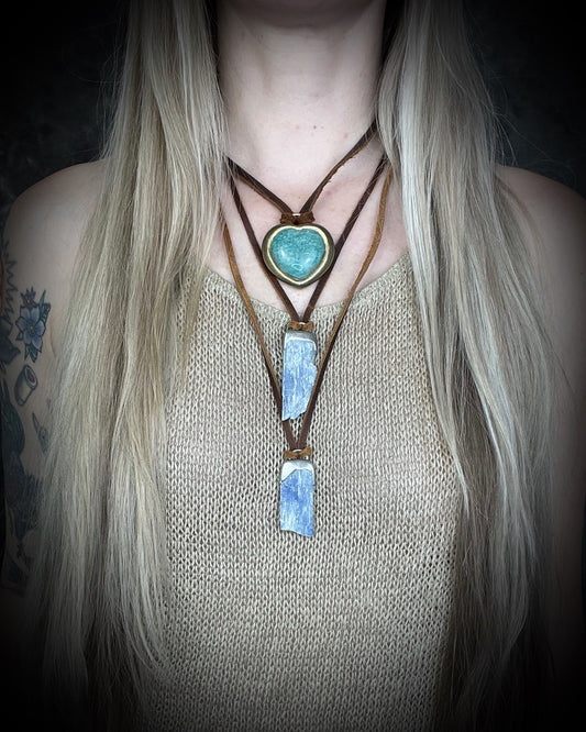 Person wearing a necklace with a heart-shaped turquoise amazonite pendant and layered rectangular blue kyanite stones, all hung from earthy brown leather and perfect for gifting!