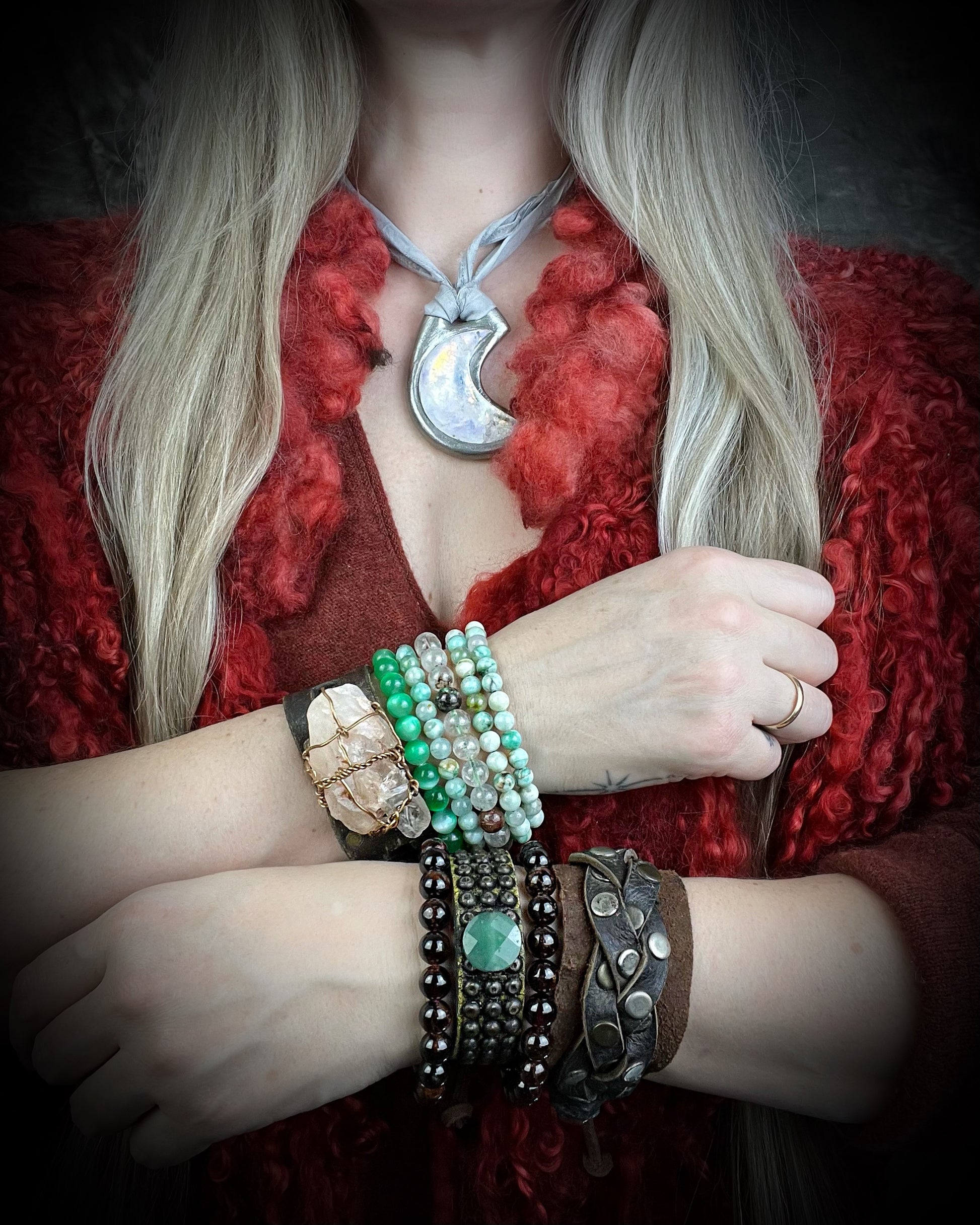 Person wearing a red garment with a necklace and multiple bracelets on a dark background