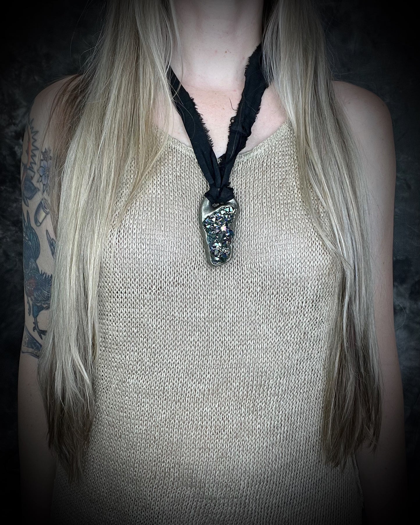 Person wearing a sparkling titanium aura amethyst pendant necklace with black recycled silk cord against a dark background
