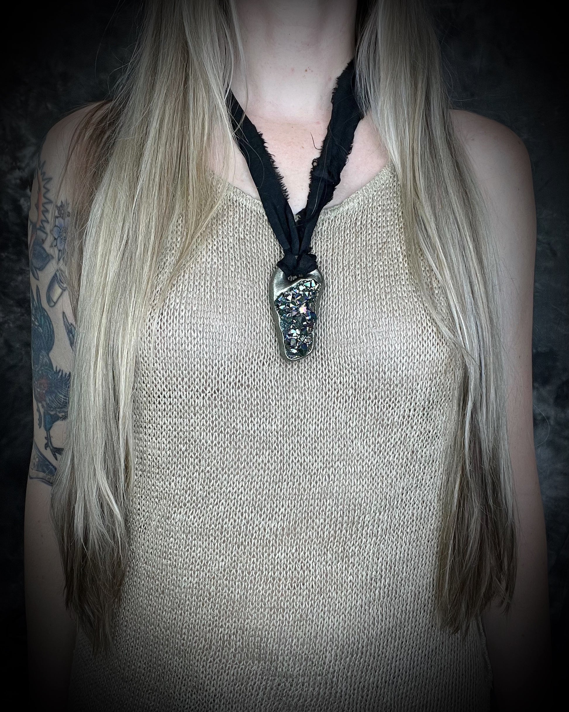 Person wearing a sparkling titanium aura amethyst pendant necklace with black recycled silk cord against a dark background