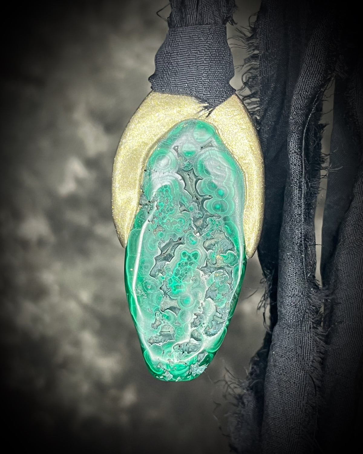 Polished malachite freeform crystal with natural green bands in a sculptural gold-finish talisman setting on black recycled silk, handmade by Become Spellbound in Baltimore, Maryland.
