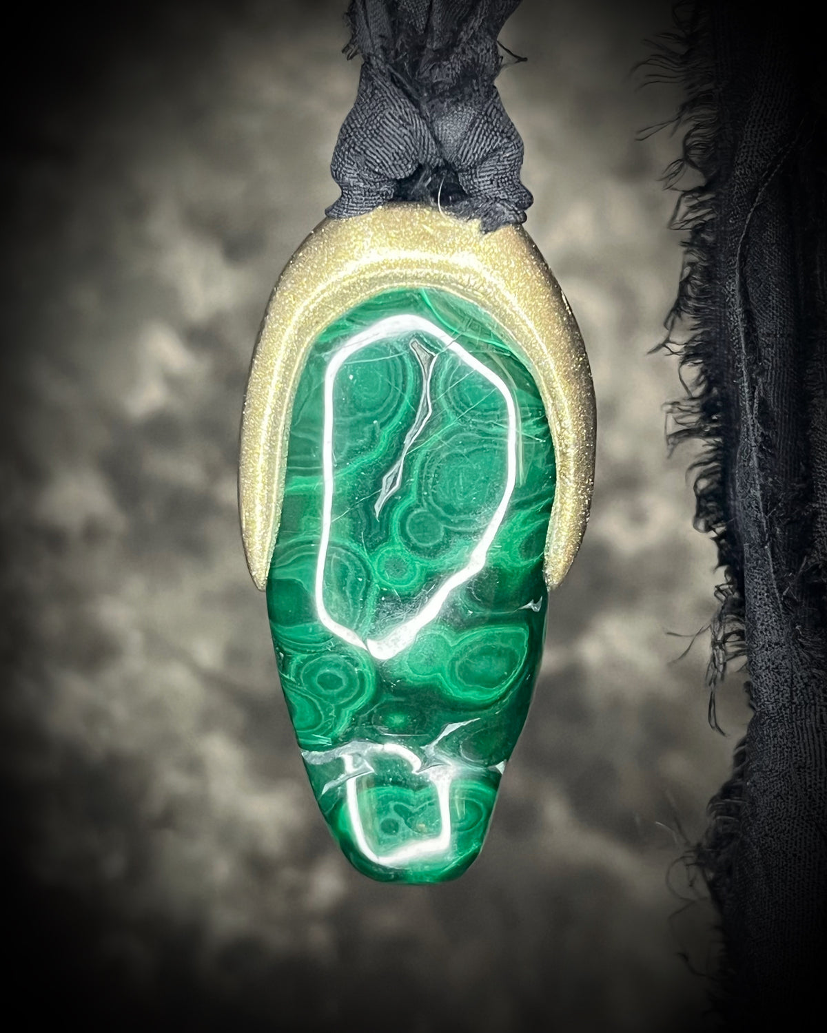 Polished malachite freeform crystal with natural green bands in a sculptural gold-finish talisman setting on black recycled silk, handmade by Become Spellbound in Baltimore, Maryland.