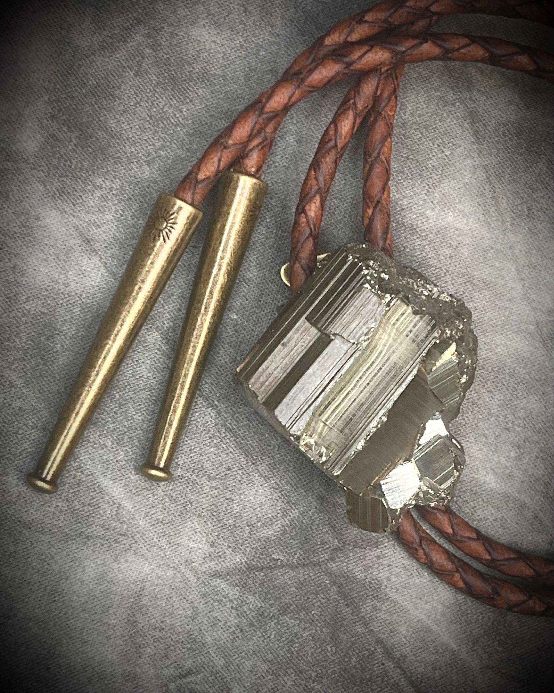 Pyrite bolo tie necklace on brown leather with gold tone finish and brass bolo tips, Western style men’s statement jewelry with natural pyrite crystal, handmade in Baltimore Maryland.