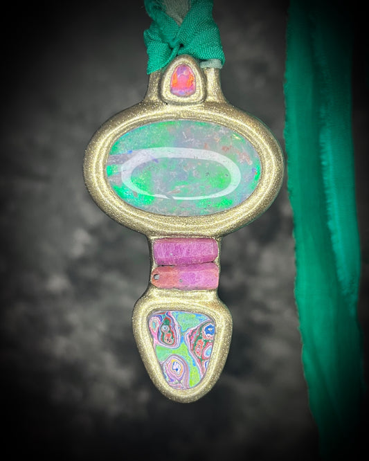 Quartz crystal doublet talisman with a mystical green glow, ruby stack, hand-cut Cadillac Ranch Fordite cabochon, and pink tourmaline crystal in a gold-finish setting on green recycled silk cords, handmade by Become Spellbound in Baltimore, Maryland.