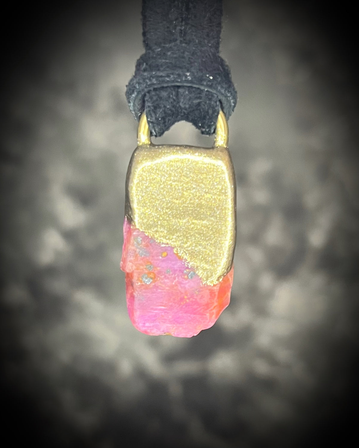 Raw ruby crystal talisman with natural texture in a sculptural gold-finish setting on black leather, handmade by Become Spellbound in Baltimore, Maryland.