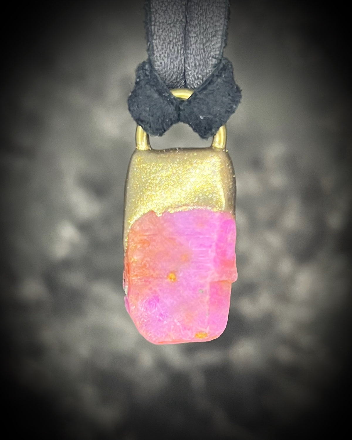 Raw ruby crystal talisman with natural texture in a sculptural gold-finish setting on black leather, handmade by Become Spellbound in Baltimore, Maryland.