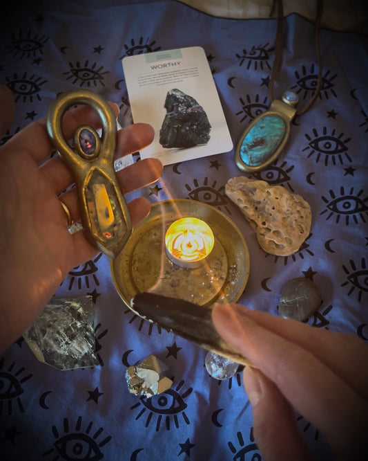 Hands holding a crystal over a lit candle with tarot cards and stones on a patterned cloth. Distance Reiki plus energetic talisman creation session. Manifestation of your energy into a custom wearable crystal or fossil talisman. 