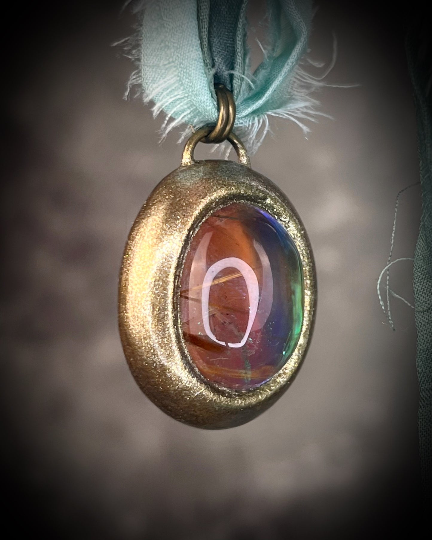 Rutilated quartz crystal talisman with sculpted gold finish, luminous green opalescent color shift, and aqua recycled silk ties. Handmade by Become Spellbound.