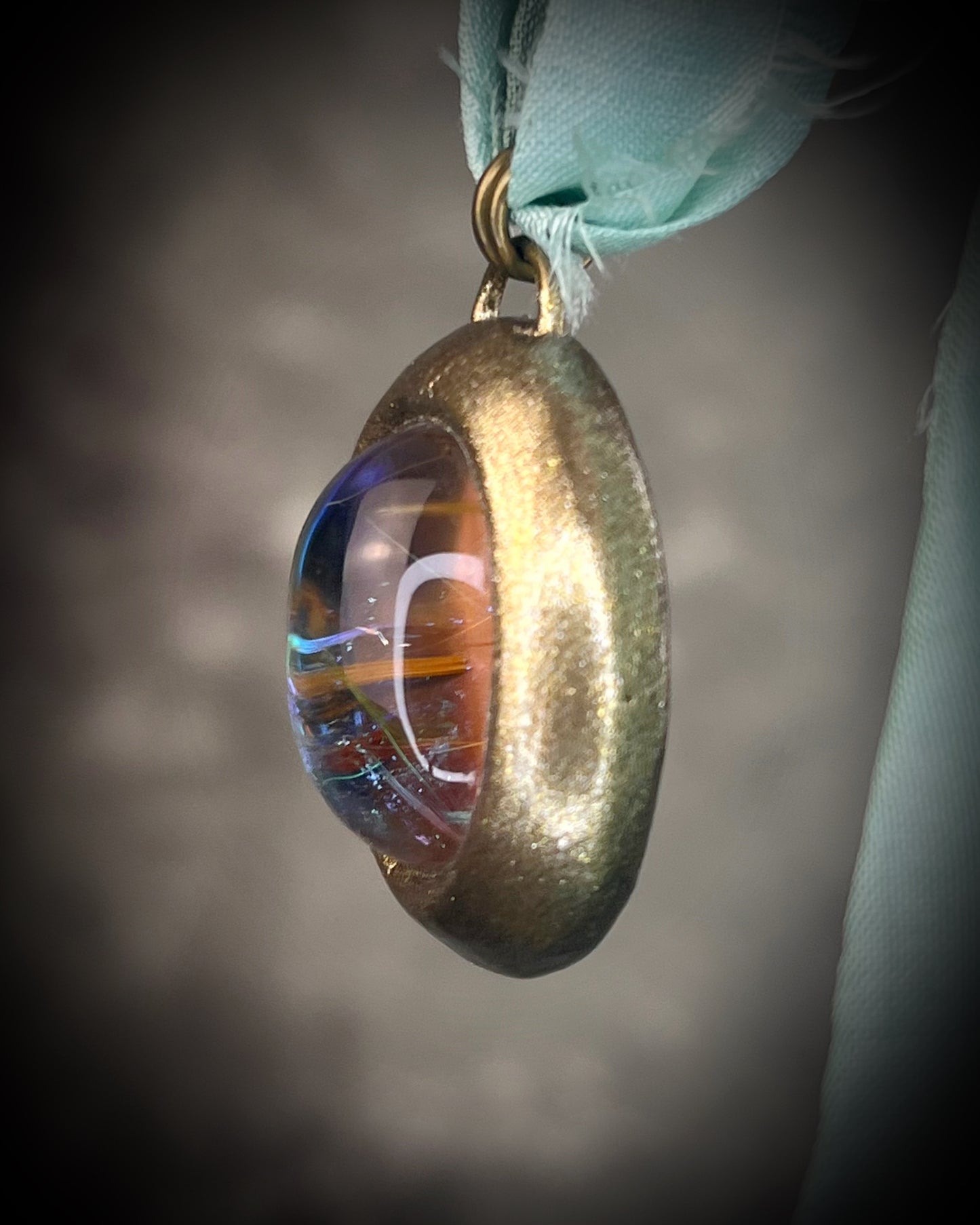 Rutilated quartz crystal talisman with sculpted gold finish, luminous green opalescent color shift, and aqua recycled silk ties. Handmade by Become Spellbound.