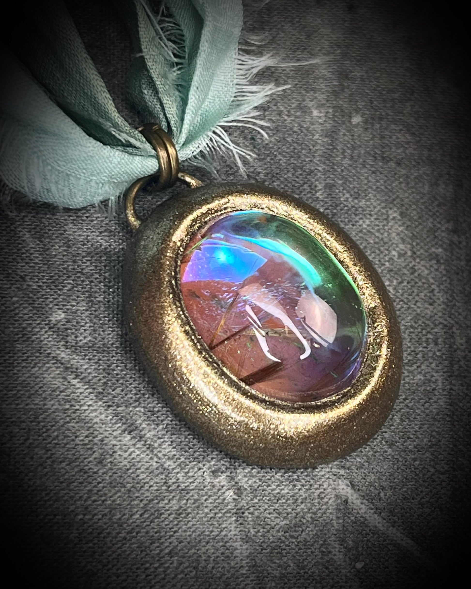 Rutilated quartz crystal talisman with sculpted gold finish, luminous green opalescent color shift, and aqua recycled silk ties. Handmade by Become Spellbound.