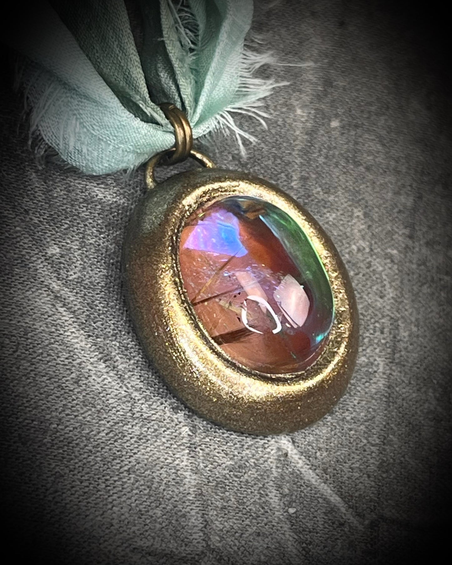 Rutilated quartz crystal talisman with sculpted gold finish, luminous green opalescent color shift, and aqua recycled silk ties. Handmade by Become Spellbound.