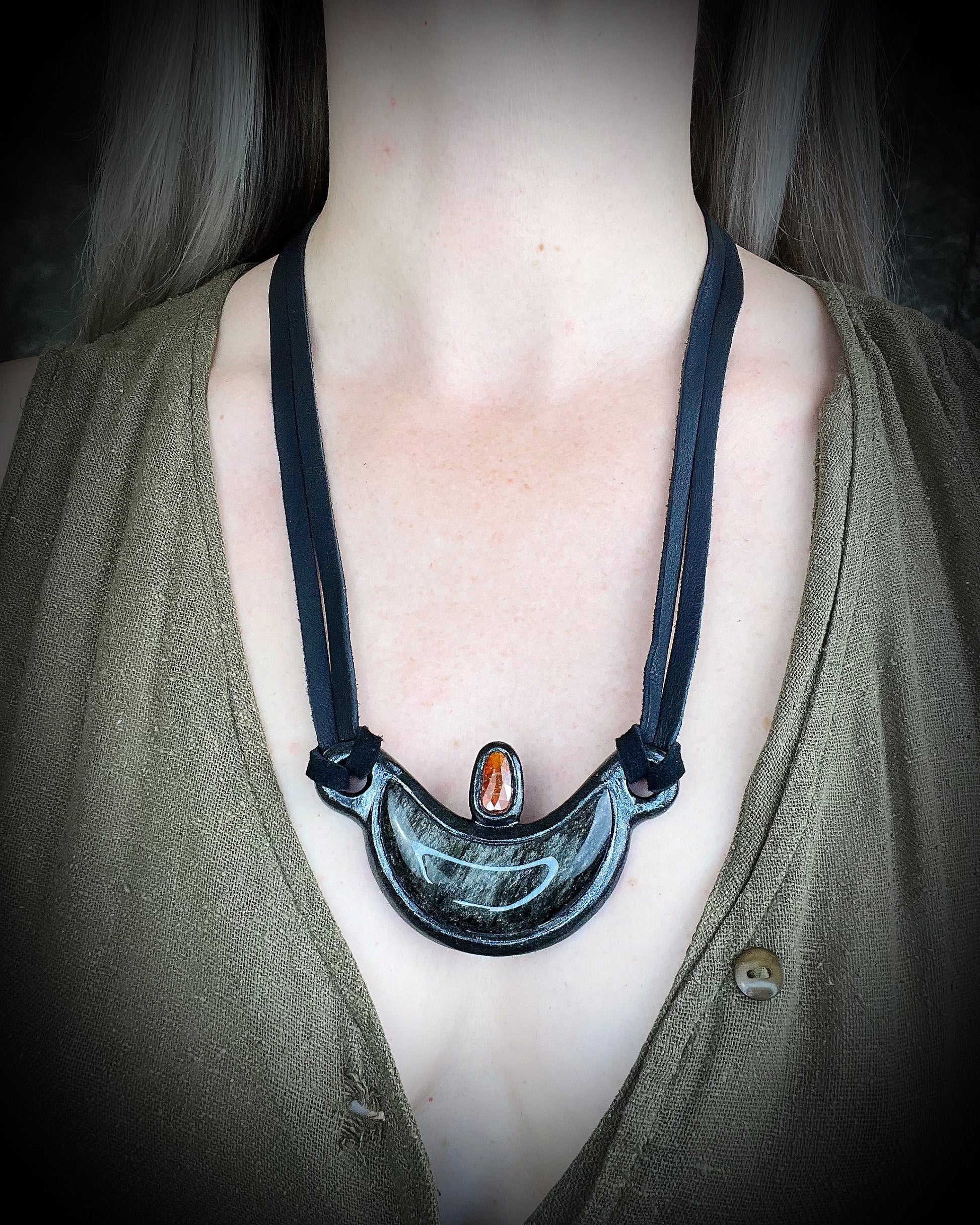 Silver Sheen obsidian crescent moon necklace with orange kyanite crystal.  Dark luxury vibe gemstone necklace hung from black leather for a unisex goth look.  