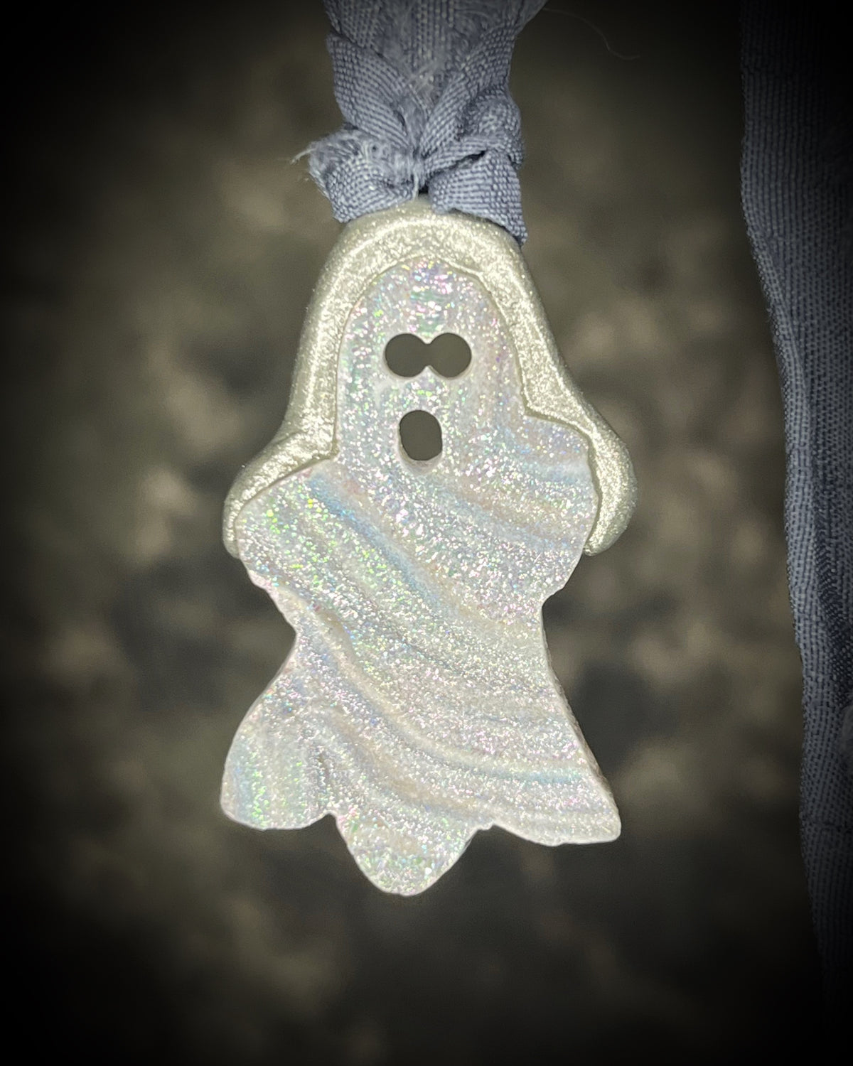 Small aura chalcedony ghost crystal carving with an iridescent glow in a sculptural silver-finish setting on dark gray recycled silk cords, handmade by Become Spellbound in Baltimore, Maryland.