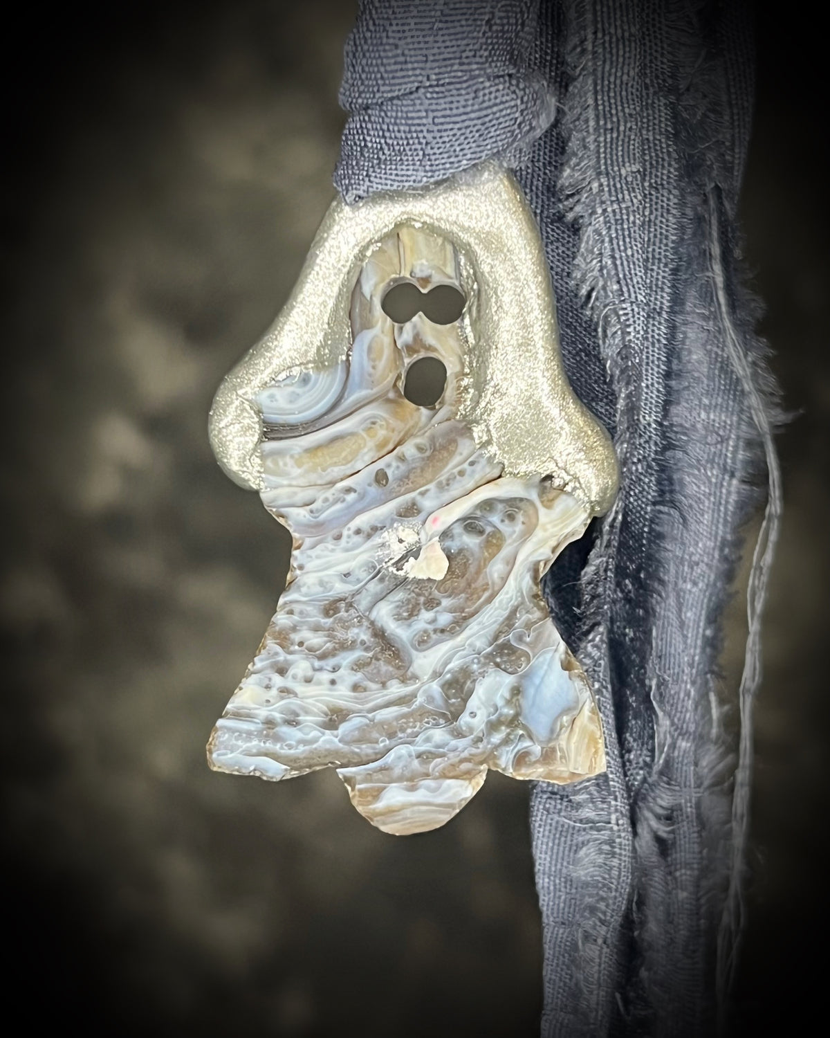 Small aura chalcedony ghost crystal carving with an iridescent glow in a sculptural silver-finish setting on dark gray recycled silk cords, handmade by Become Spellbound in Baltimore, Maryland.