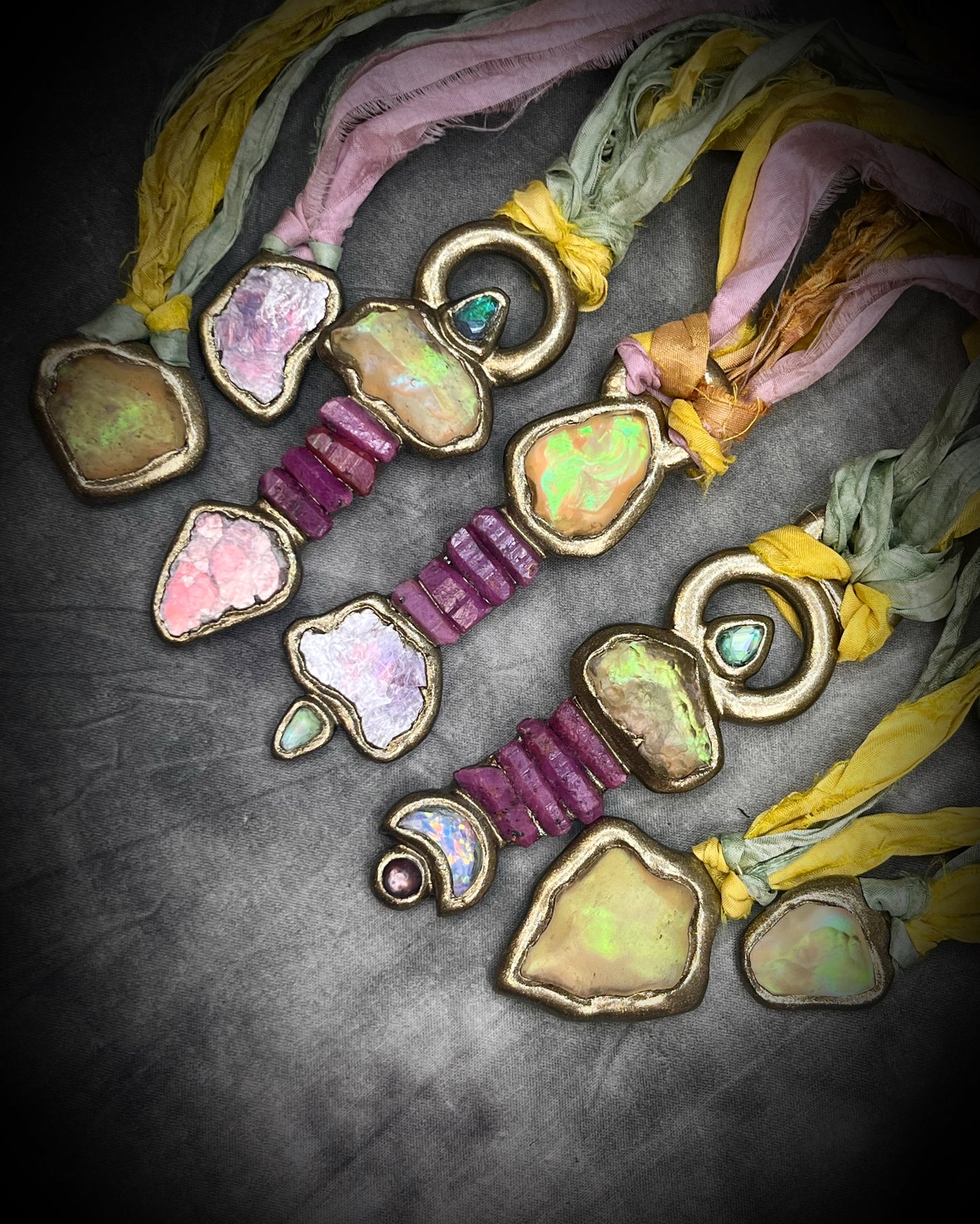 Starborn collection crystal jewelry display. Handmade Libyan Desert Glass talisman necklaces with raw ruby crystals, lepidolite, green tourmaline, and recycled silk ties featuring luminous shifting flashes of color.