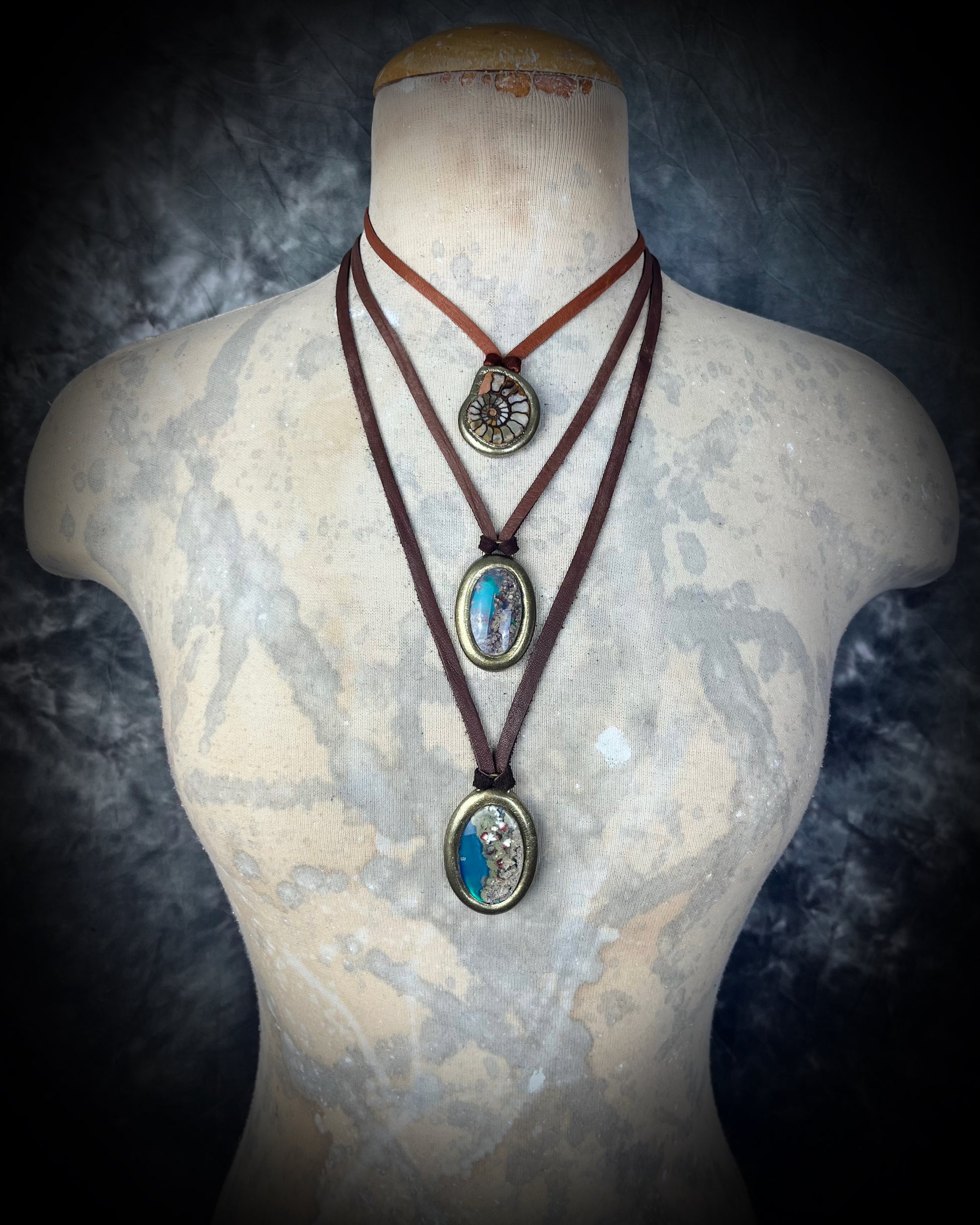 Three-layered necklaces featuring ammonite fossil and scenic quartz crystal on a mannequin bust against a dark background.