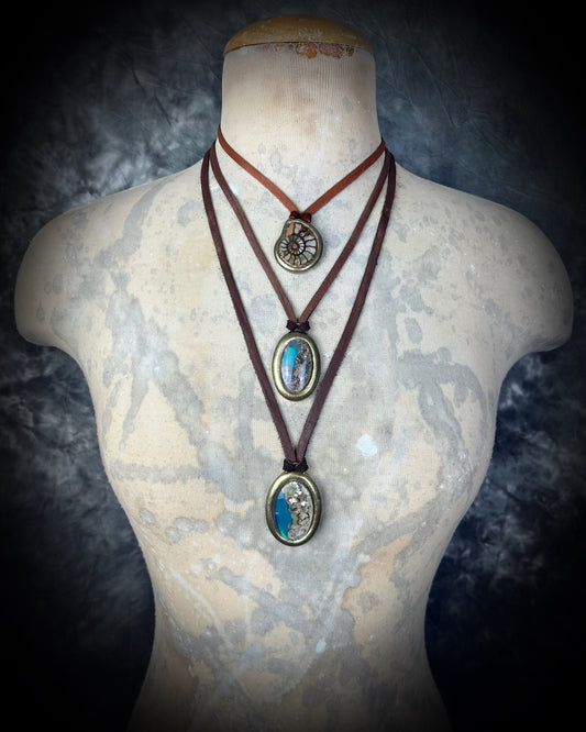 Three-layered necklaces featuring ammonite fossil and scenic quartz crystal on a mannequin bust against a dark background.