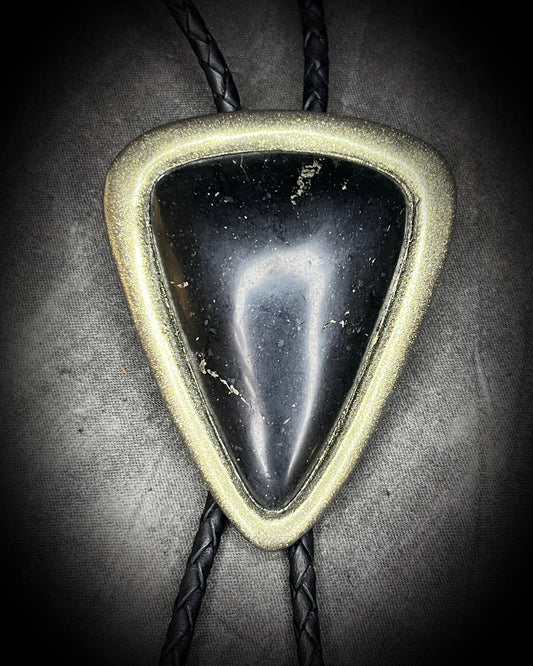 Triangular stone pendant bolo tie on a braided black leather cord against a dark background. Detail view of raw Black Tourmaline crystal with gold finish