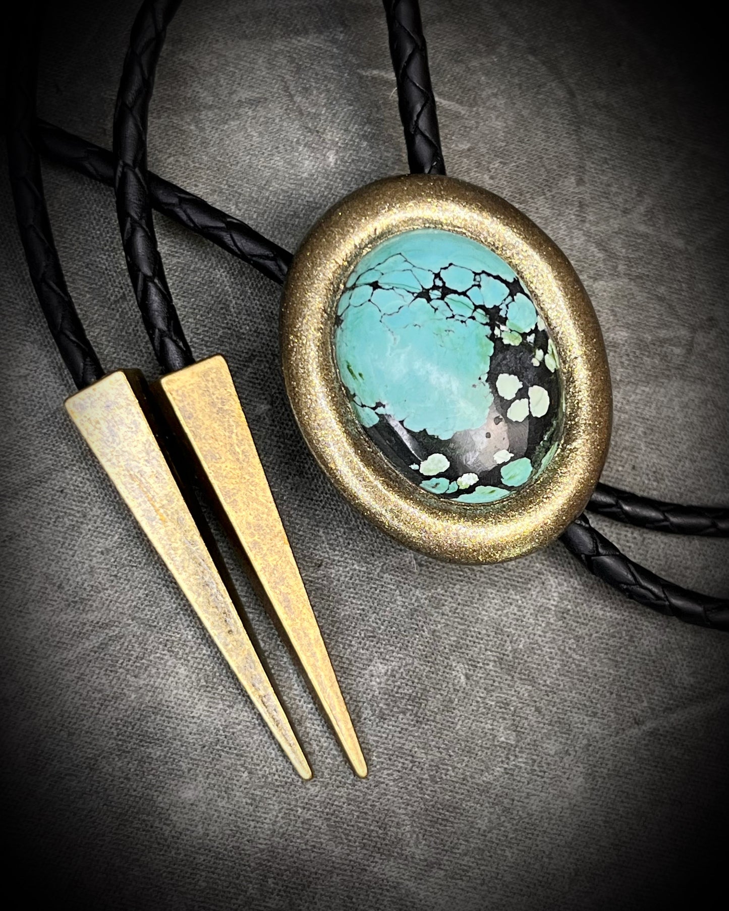 Turquoise bolo tie necklace in gold finish on black leather with spike tips, artisan Western statement jewelry with crystal focal stone, handmade in Baltimore Maryland.