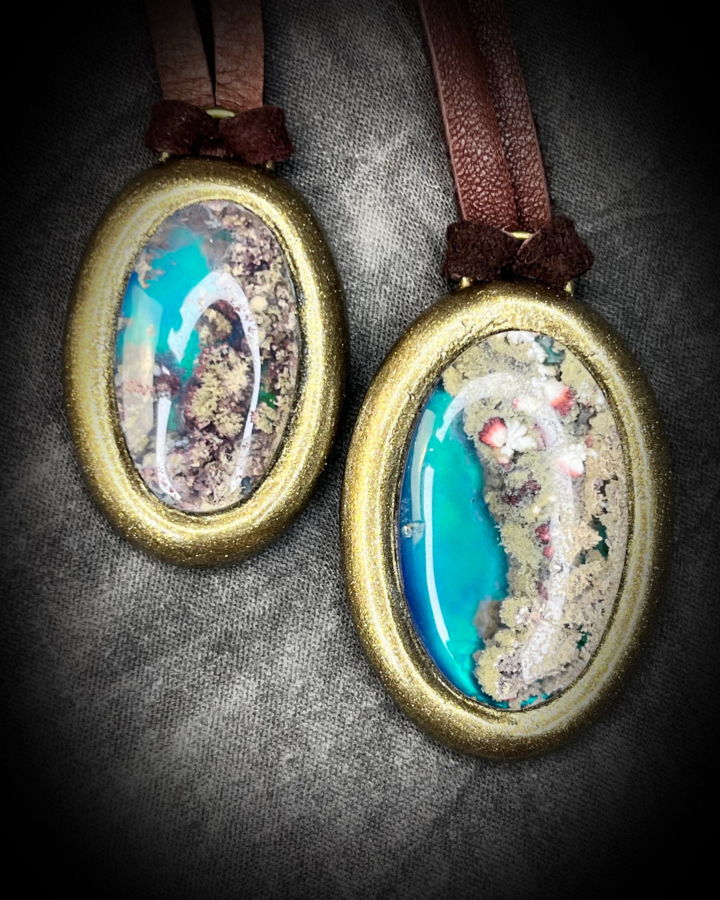 Two glowing, Scenic Moss Agate necklaces hung from earthy brown leather and styled against neutral linen background.