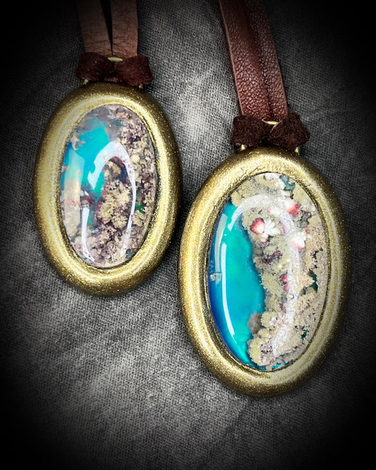 Two glowing, Scenic Moss Agate necklaces hung from earthy brown leather and styled against neutral linen background.