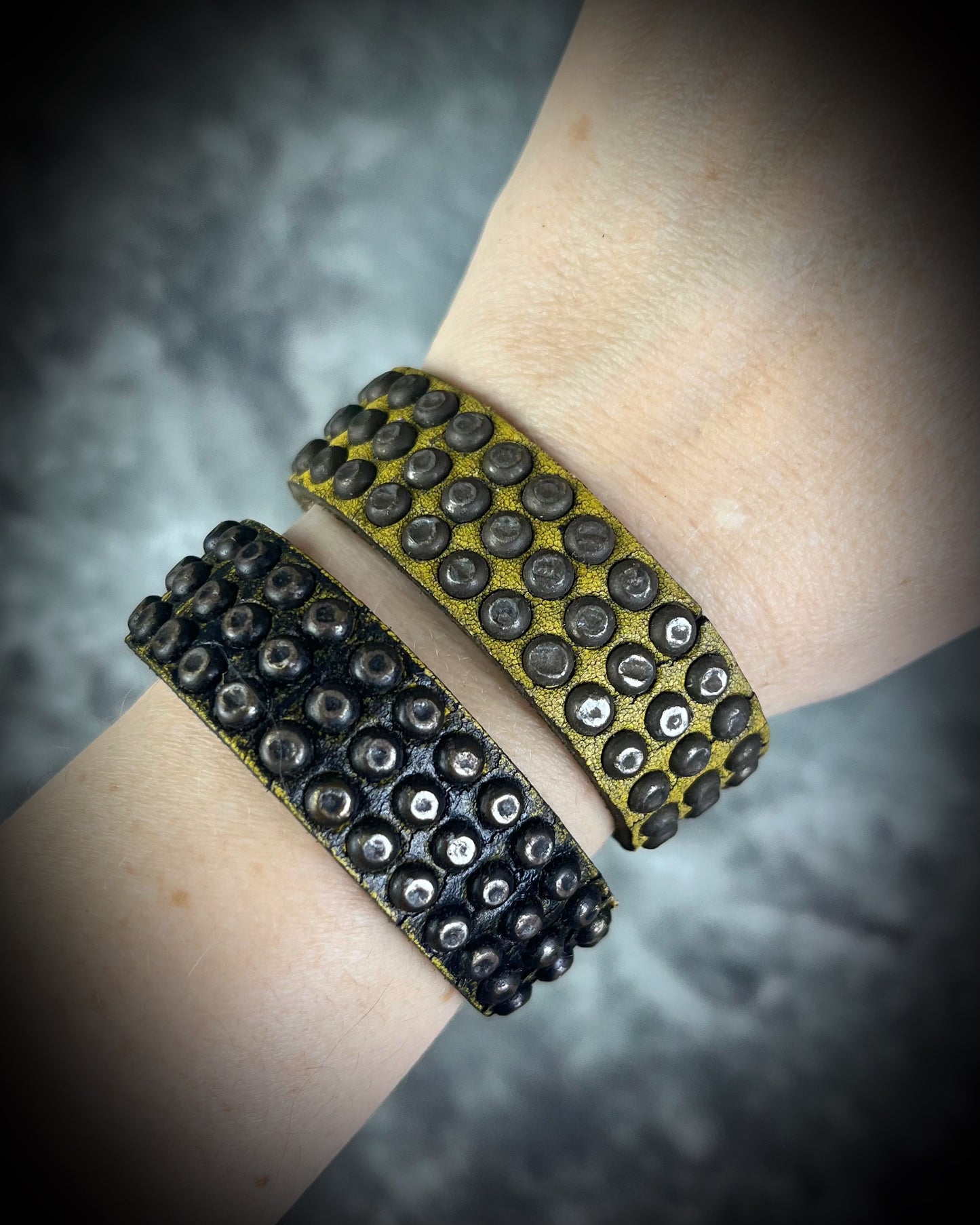 Two studded handmade leather bracelets worn layered on a wrist. Unisex rugged leather cuff jewelry.