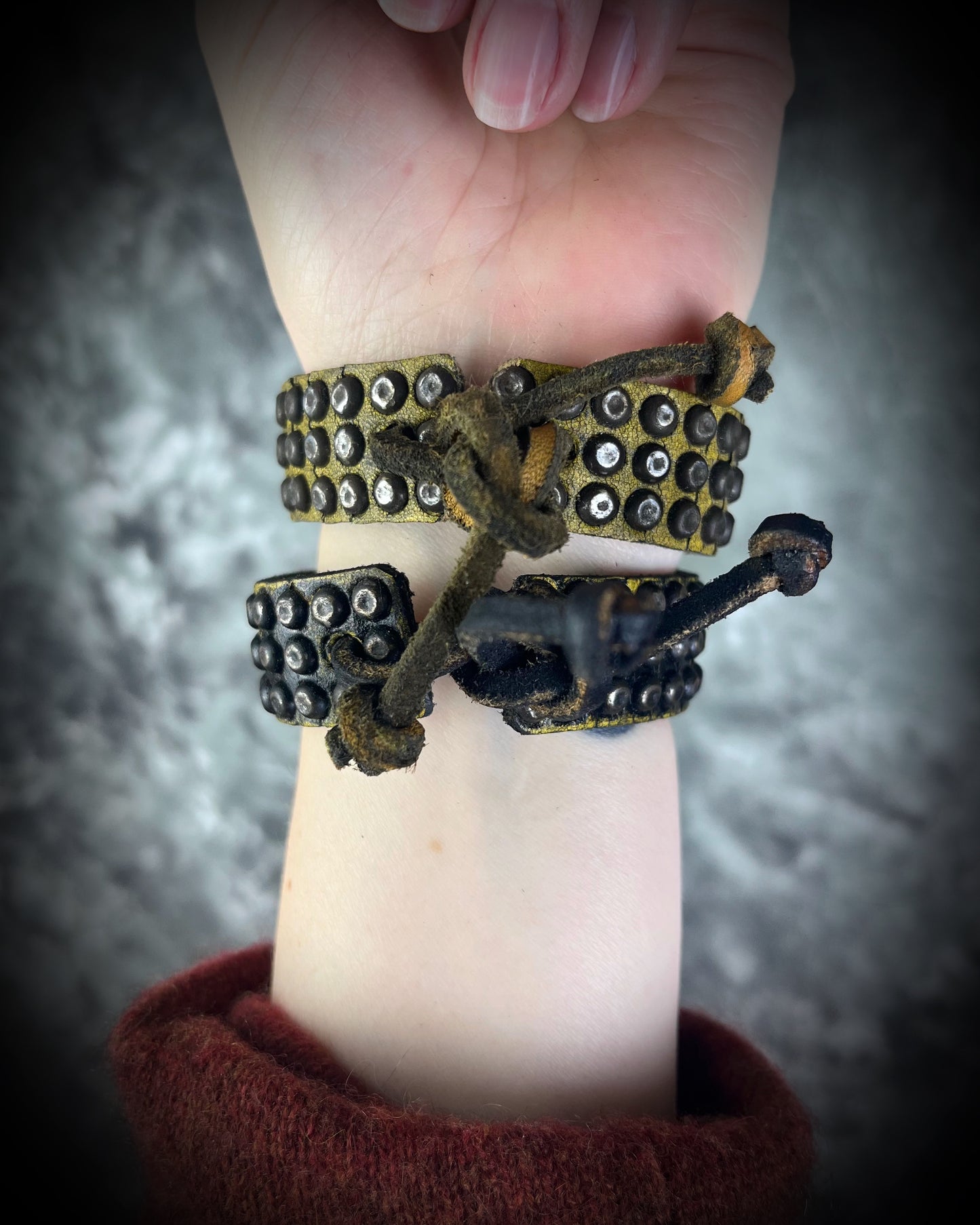 Two studded handmade leather bracelets worn layered on a wrist. Unisex rugged leather cuff jewelry shown here the tie back.