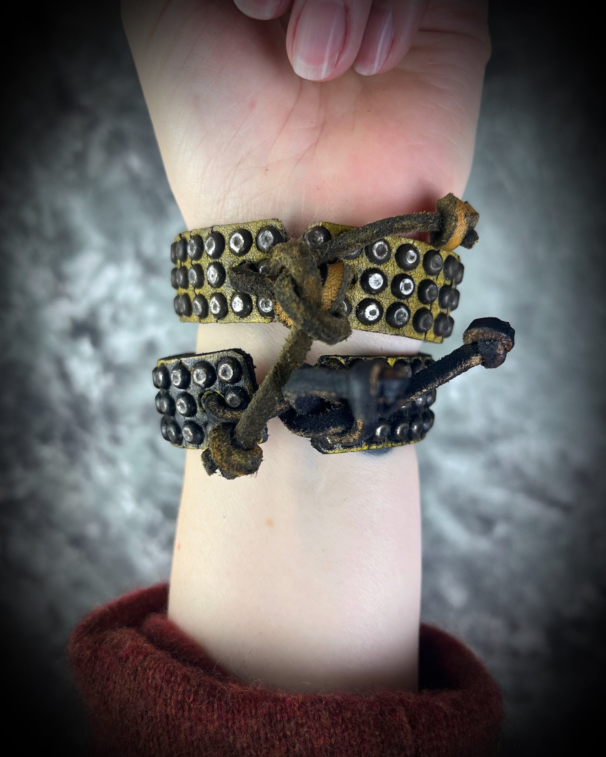 Two studded handmade leather bracelets worn layered on a wrist. Unisex rugged leather cuff jewelry shown here the tie back.