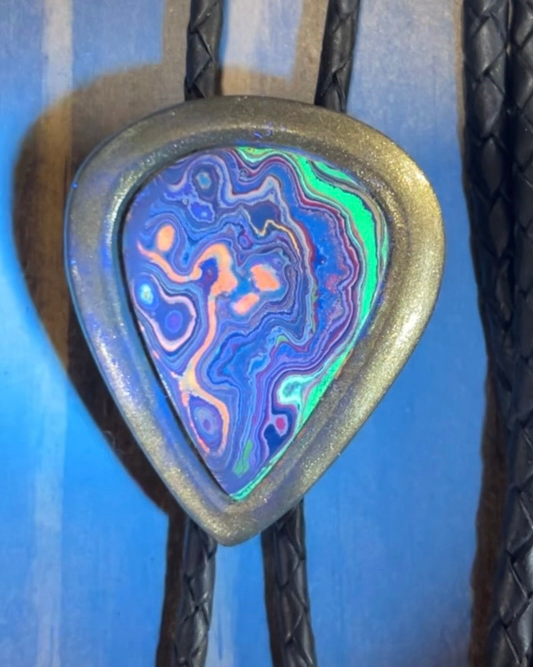 Cadillac Ranch Fordite manmade gemstone UV reactive Bolo tie set in a gold finish and mounted on soft black bolo leather. A talisman for the modern man, crystal jewelry for him. Western 2026 jewelry trend bolo. 