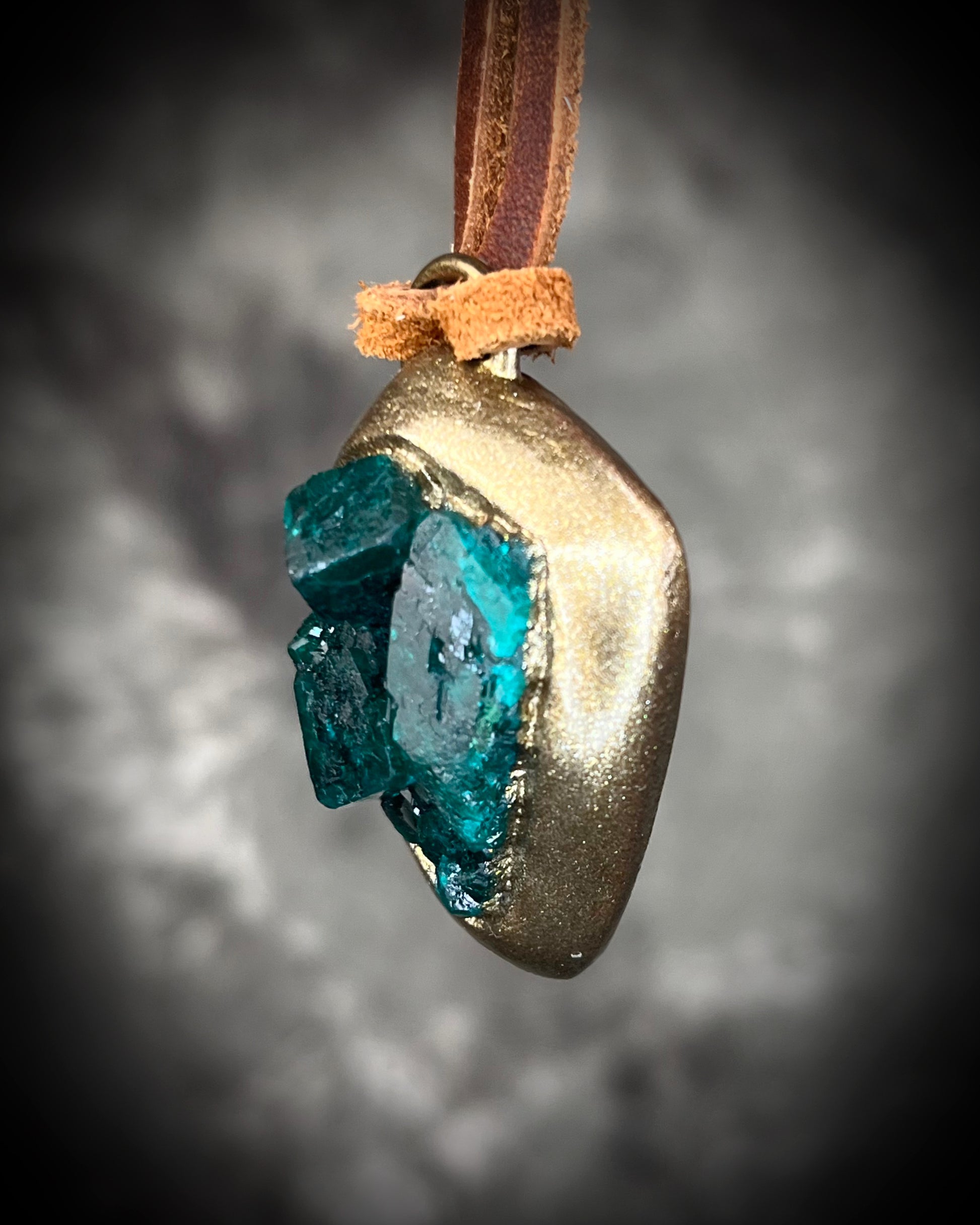 Vivid emerald green chunky dioptase crystal pendant handmade and set in a gold finish, hung from soft brown leather for an earthy, unisex vibe. Jewery for men or gift for her. Side view.