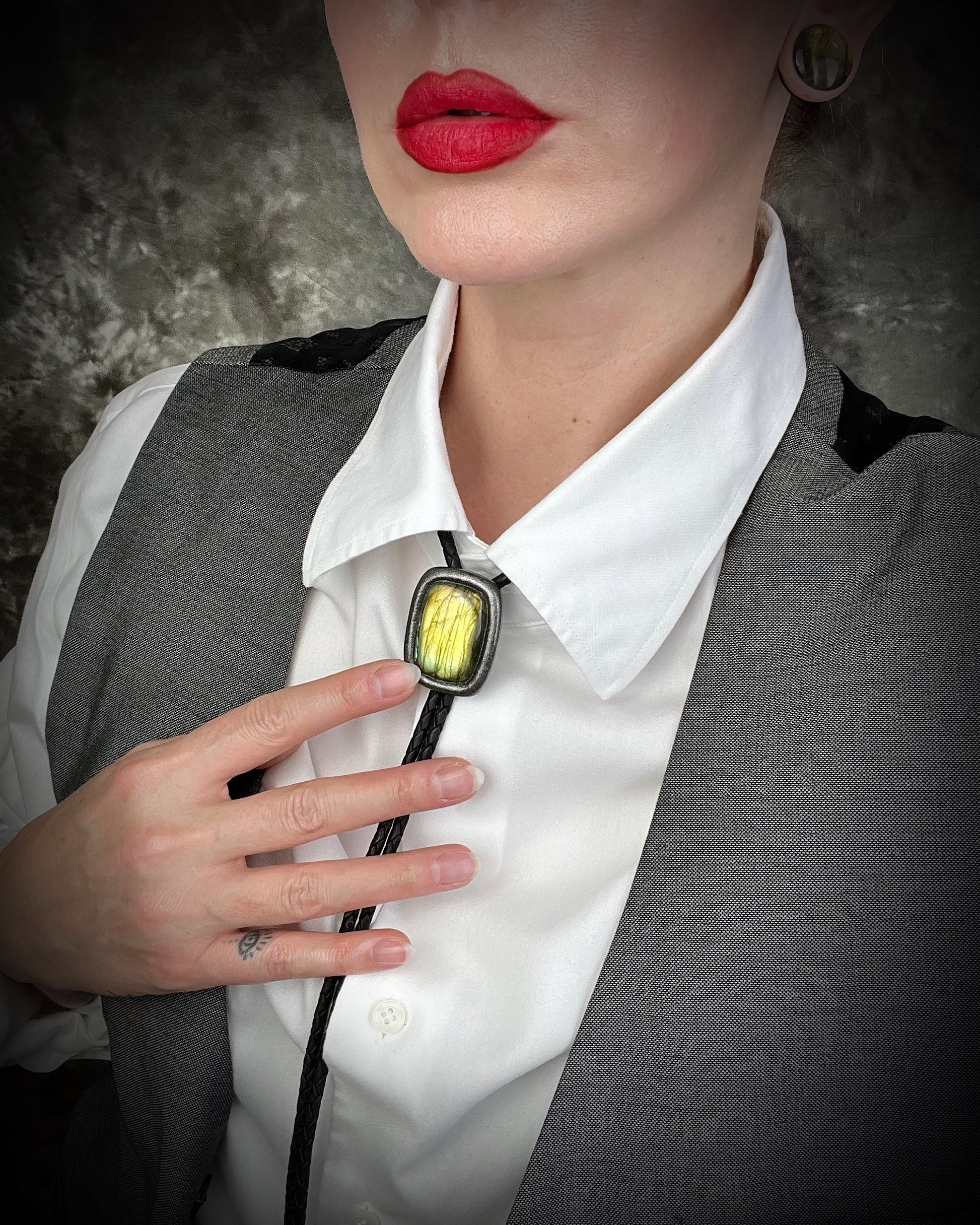 Person wearing a white shirt, gray vest, and holding a bolo tie with a yellow stone.