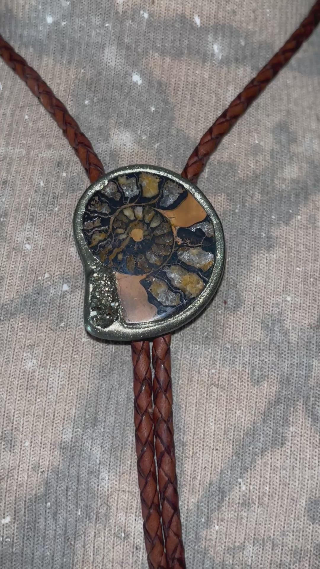 Close-up video of ammonite spiral with golden pyrite crystal — artisan bolo necklace with brass gold tips.