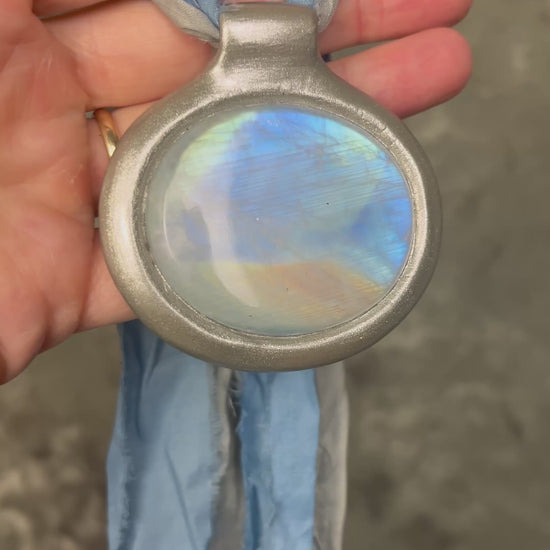XL rainbow moonstone fire pendant handmade in a silver finish for moon goddess energy. Hung from blue and silver recycled silk for an ethereal and intuitive energy. Spiritual summer jewelry gift for her. 