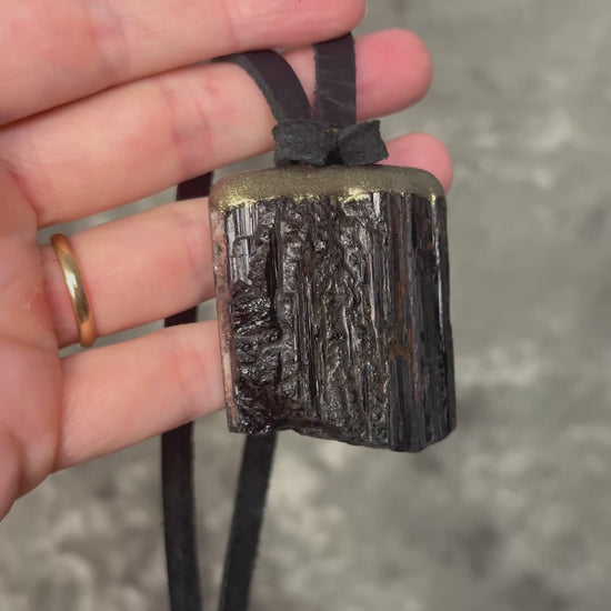 Gold finish, square shaped raw stone Black tourmaline grounding and protection pendant hung from black leather for an earthy adornment. Open back to touch skin and ground you. 