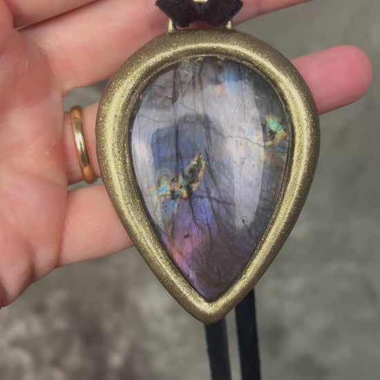 Purple flash moody violet labradorite teardrop crystal necklace in a gold finish on black leather. Handmade mystical jewelry statement pendant for her. 