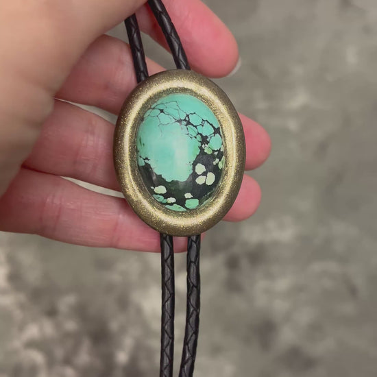 Turquoise bolo tie necklace in gold finish on black leather with spike tips, artisan Western statement jewelry with crystal focal stone, handmade in Baltimore Maryland.